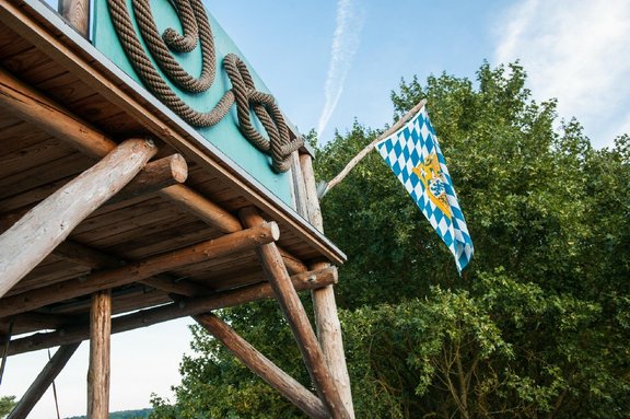 Eine Ecke vom Lagerturm aus Holz mit bayerischer Fahne und der Bucher Berg Schnecke aus Schiffstau auf ein Brett montiert 
