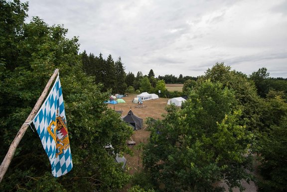 Im Bildvordergrund hängt eine bayerische Fahne, im Hintergrund sind Zelte auf der Wiese zu sehen
