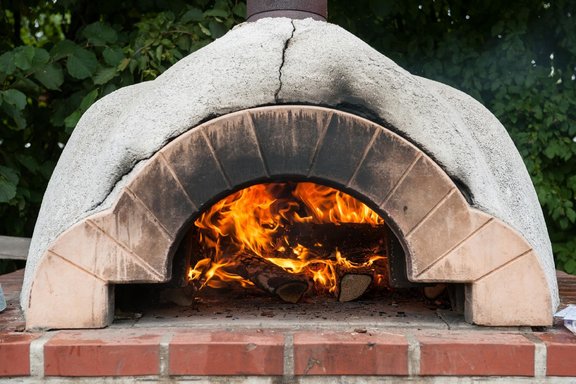 ein weißer gemauerter Pizzaofen, in dem ein Feuer brennt