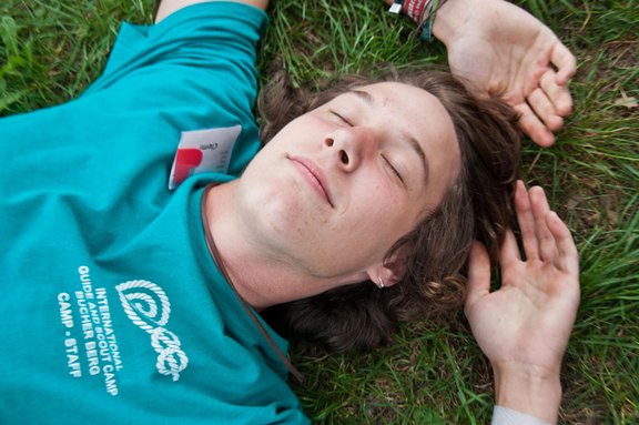 Junge mit türkisem Staff-T-Shirt liegt mit geschlossenen Augen im Gras und träumt